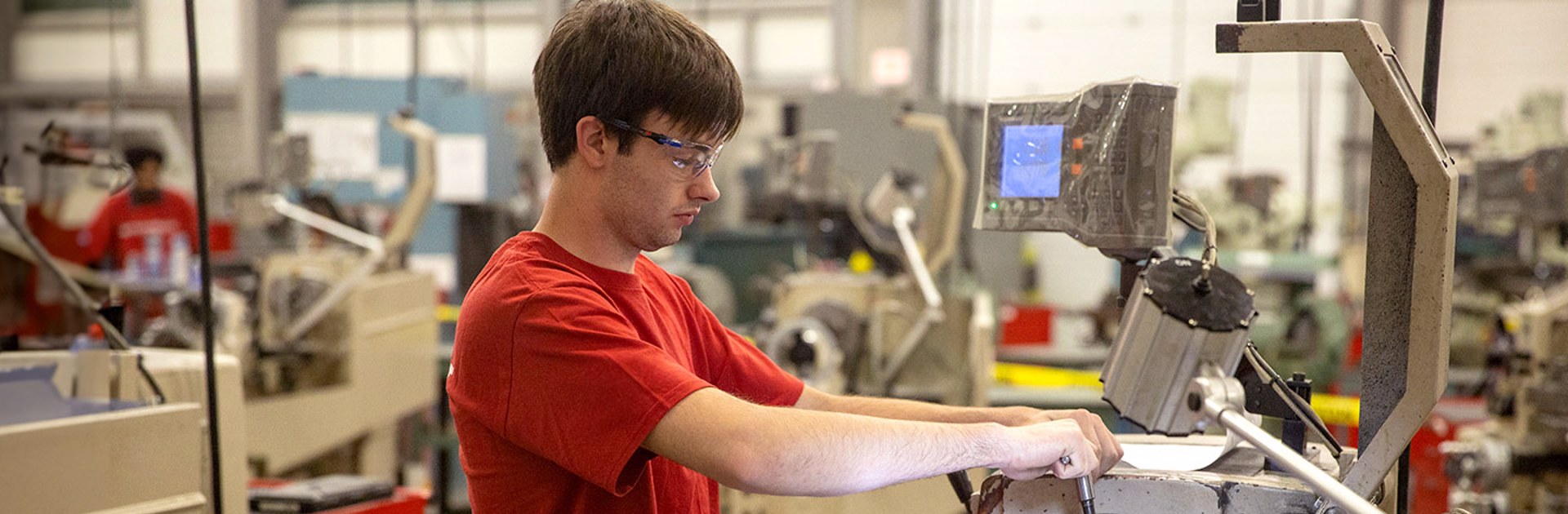 Trades student in a college classroom using an automatic electrical welding tool